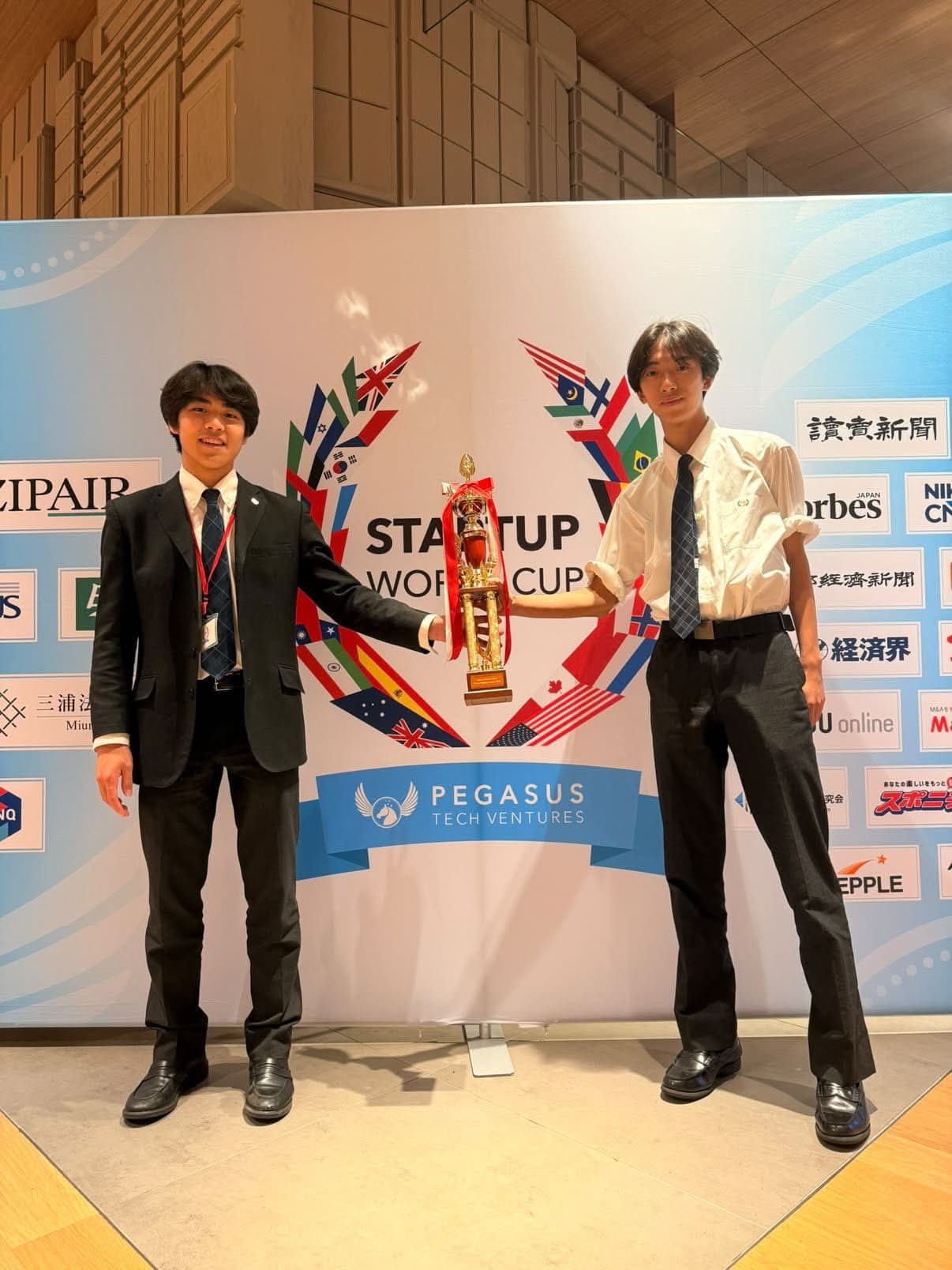 Startup World Cupのパネルの前で、トロフィーを持つBlescのメンバー2人